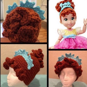 May include: Crocheted brown hat with a light blue trim, resembling a dinosaur's head. The hat is handmade and features a textured design. The image also shows a doll wearing a similar hat.