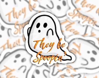 May include: A white ghost sticker with black outlines and facial features, featuring the orange text "They be Spoopin'" centered on the body. The ghost has two oval eyes and a small circular mouth, with a rounded top and a trailing tail shape.