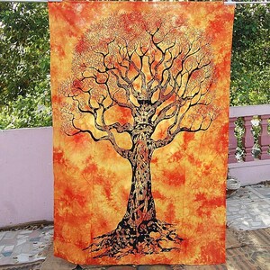 May include: A large, orange tapestry with a detailed black tree design. The tree's branches and roots are intricately drawn against a vibrant, textured background. The tapestry is hanging outdoors, showcasing its decorative nature.