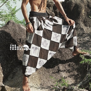 Puede incluir: Un hombre con rastas que lleva pantalones de patrón blanco y negro con un diseño geométrico. Los pantalones son holgados y tienen una pierna ancha. El hombre está de pie sobre una gran roca.