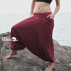 Puede incluir: Una mujer con un top bandeau negro y pantalones de harén marrones se para en una roca junto al mar. Los pantalones tienen un bolsillo grande en el lado derecho.