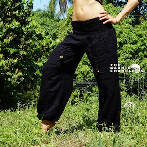 May include: A woman wearing a black hat, a green crop top, and black trousers with a drawstring waist. She is standing in a grassy area with trees in the background.