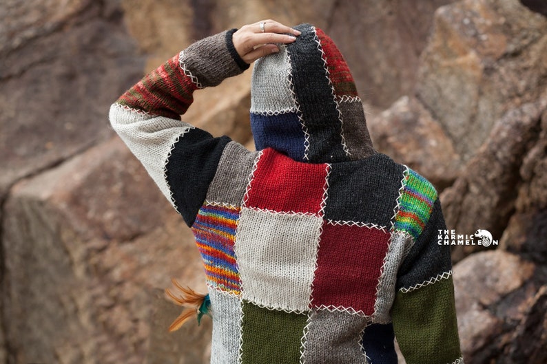 May include: A patchwork hooded sweater with a variety of colors, including red, blue, green, and white. The sweater is made of knitted fabric and has a loose fit.