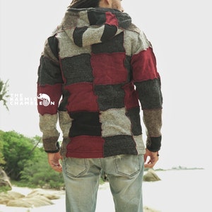 May include: A patchwork hoodie in shades of gray, black, and burgundy. The hooded jacket has a unique design with a mix of square patches. The Karmic Chameleon logo is visible on the left side. The person is wearing light blue jeans.