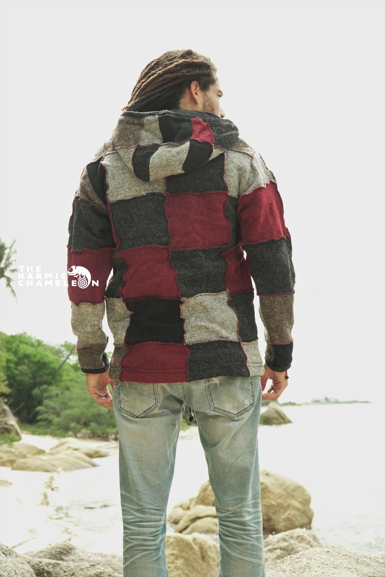 May include: A patchwork hoodie in shades of gray, black, and burgundy. The hooded jacket has a unique design with a mix of square patches. The Karmic Chameleon logo is visible on the left side. The person is wearing light blue jeans.