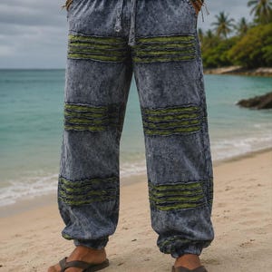 May include: Acid-washed blue denim pants featuring horizontal olive green distressed fabric panels, an elasticized waistband with a drawstring closure, and cuffed ankles. The pants have a loose, relaxed fit with side pockets and a textured finish.