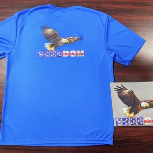 May include: A blue t-shirt with a graphic of a bald eagle flying with the word "FREEDOM" printed in red, white, and blue.