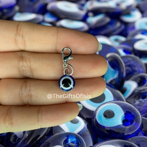 May include: A silver charm with a blue evil eye bead. The charm is attached to a silver lobster clasp. The charm is surrounded by many other blue evil eye beads.