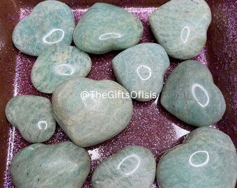 May include: A selection of heart-shaped amazonite stones in a range of sizes. The stones are a pale turquoise hue with delicate veining. They are displayed in a wooden tray with a glittery pink interior. The text "INDOOR LIGHT" is visible in the image.