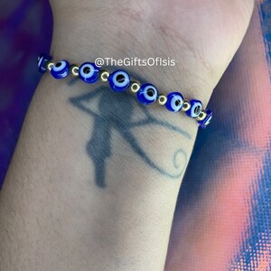 May include: A blue and gold evil eye bracelet with gold beads. The bracelet is on a person's wrist. @TheGiftsOfIsis