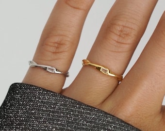 May include: A hand displays three rings: a silver ring with a rectangular stone, a gold ring with a rectangular stone, and a gold ring with a purple stone. The rings are on a hand with light purple nail polish.