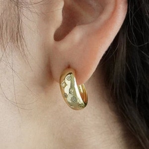 May include: Gold hoop earrings with a textured surface. The earrings are worn in a person's ear.