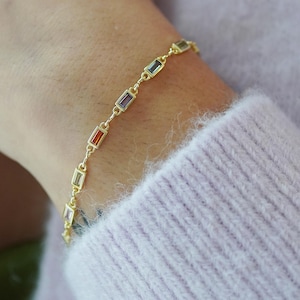 May include: A gold chain bracelet with colourful rectangular gemstones. The bracelet is on a person's wrist.