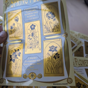May include: A set of gold foil stickers featuring illustrations of spring flowers and quotes about flowers. The quotes are by Claude Monet and Frida Kahlo. The stickers are on a white background with a gold border. The text on the stickers reads: "I must have flowers, always and always." - Claude Monet and "I paint flowers so they will not die." - Frida Kahlo.