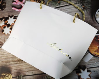 May include: White gift bag with gold rope handles and the word "fabulous" written in gold lettering.