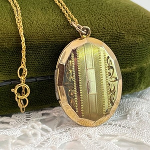 May include: A gold oval locket pendant on a fine chain. The locket has a detailed pattern of vertical lines and floral motifs. It is presented against a green velvet backdrop, highlighting its antique style and design.