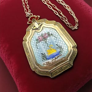 May include: Vintage gold-tone pendant necklace. The rectangular pendant displays a painted scene of a yellow swan on blue water, pink roses, and a light blue background. The necklace has a long chain.