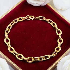 May include: A gold chain bracelet featuring a series of interlocking oval links. Each individual link displays a fine, textured cross-hatch pattern on its surface. The bracelet is secured with a circular spring ring clasp mechanism at the top.