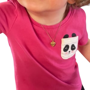 May include: A bright pink t-shirt with a panda bear pocket design. The shirt features a gold heart-shaped pendant necklace. The panda pocket has a white background with a black and white panda face.