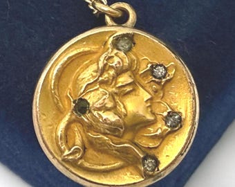 Puede incluir: Un collar con colgante dorado con un relieve detallado del perfil de una mujer. El colgante redondo está adornado con pequeñas piedras preciosas brillantes. La cadena dorada completa esta joya clásica y elegante.