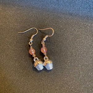 May include: A pair of silver cupcake charm earrings with pink beads. The earrings have silver hooks.