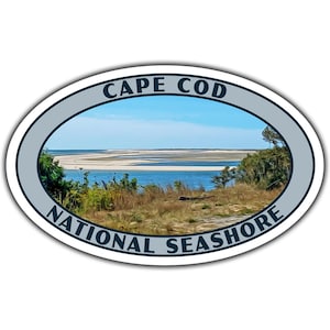 May include: Oval sticker with a blue and white design. The sticker features a scenic view of a beach with a blue sky and white clouds. The text "CAPE COD NATIONAL SEASHORE" is printed in a dark blue font around the image.