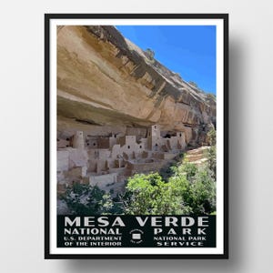 May include: A framed poster featuring the cliff dwellings of Mesa Verde National Park in Colorado. The image shows stone structures built into a canyon wall under a bright blue sky, with text at the bottom reading MESA VERDE NATIONAL PARK.