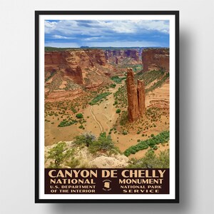 May include: A framed poster featuring a landscape illustration of Canyon de Chelly National Monument with red rock formations, green vegetation, and a blue sky. The text reads CANYON DE CHELLY NATIONAL MONUMENT U.S. DEPARTMENT OF THE INTERIOR.