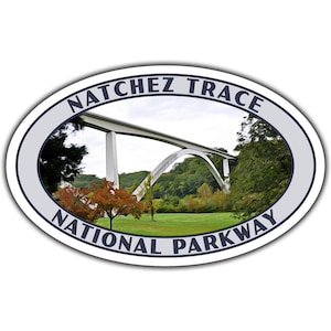 May include: A white oval sticker with blue text that reads "Natchez Trace National Parkway". The sticker features a photo of a white bridge with a green grassy field and trees in the background.