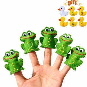 May include: Five green felt frog finger puppets with googly eyes and stitched numbers one through five. Above, a set of six small felt duck figures includes one white duck and five yellow ducks labeled with the numbers one through five and the word gift.
