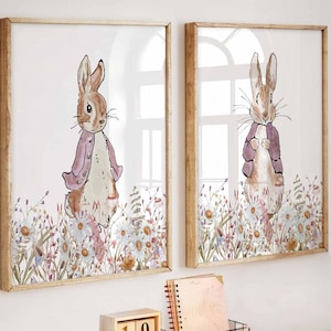 Pode incluir: Duas impressões em aquarela emolduradas de um coelho com um casaco roxo em um campo de flores. Uma mesa branca com um laptop, livros e uma vela. Um vaso de tulipas brancas e uma cadeira dourada completam a cena.