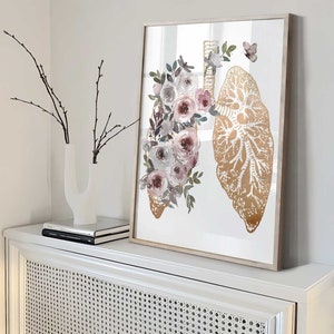 K&ouml;nnte beinhalten: Ein gerahmter Druck einer goldenen anatomischen Illustration von Lungen mit Aquarell-Rosen und wei&szlig;en Blumen und Gr&uuml;n.