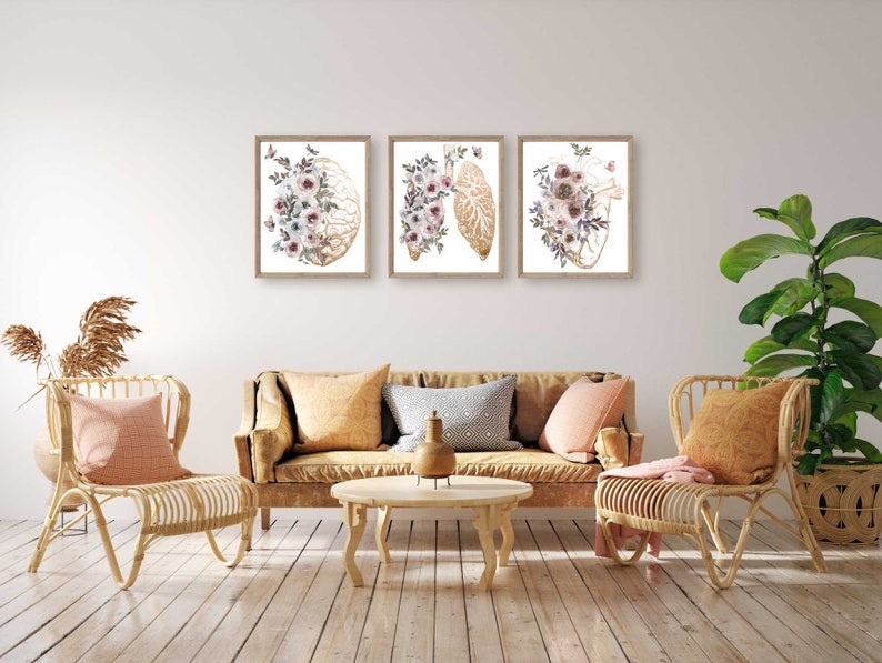 K&ouml;nnte beinhalten: Drei gerahmte Drucke mit anatomischen Illustrationen von Gehirn, Herz und Lunge, jeweils mit Aquarell-Blumenmotiven in Rosa-, Wei&szlig;- und Goldt&ouml;nen.