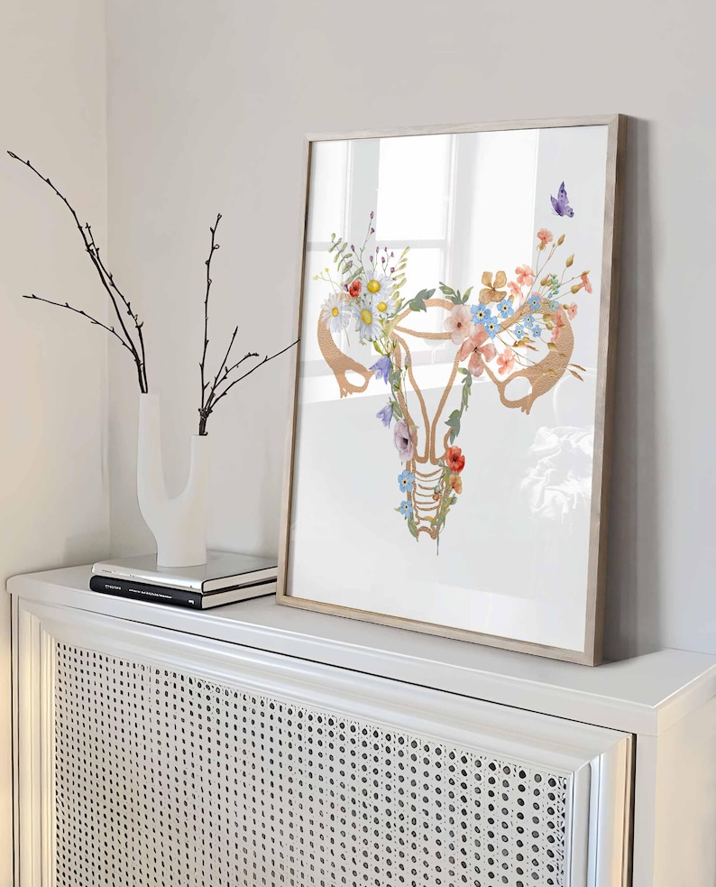 以下が含まれることがあります： ピンク、ブルー、ホワイトのウォーターカラーの花が描かれた、女性の生殖器の解剖学的イラストの額装されたプリントです。
