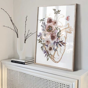 K&ouml;nnte beinhalten: Ein gerahmter Druck eines anatomischen Herzens in Aquarell mit rosa, lila und wei&szlig;en Blumen und Gr&uuml;n. Das Herz ist in Gold umrandet.