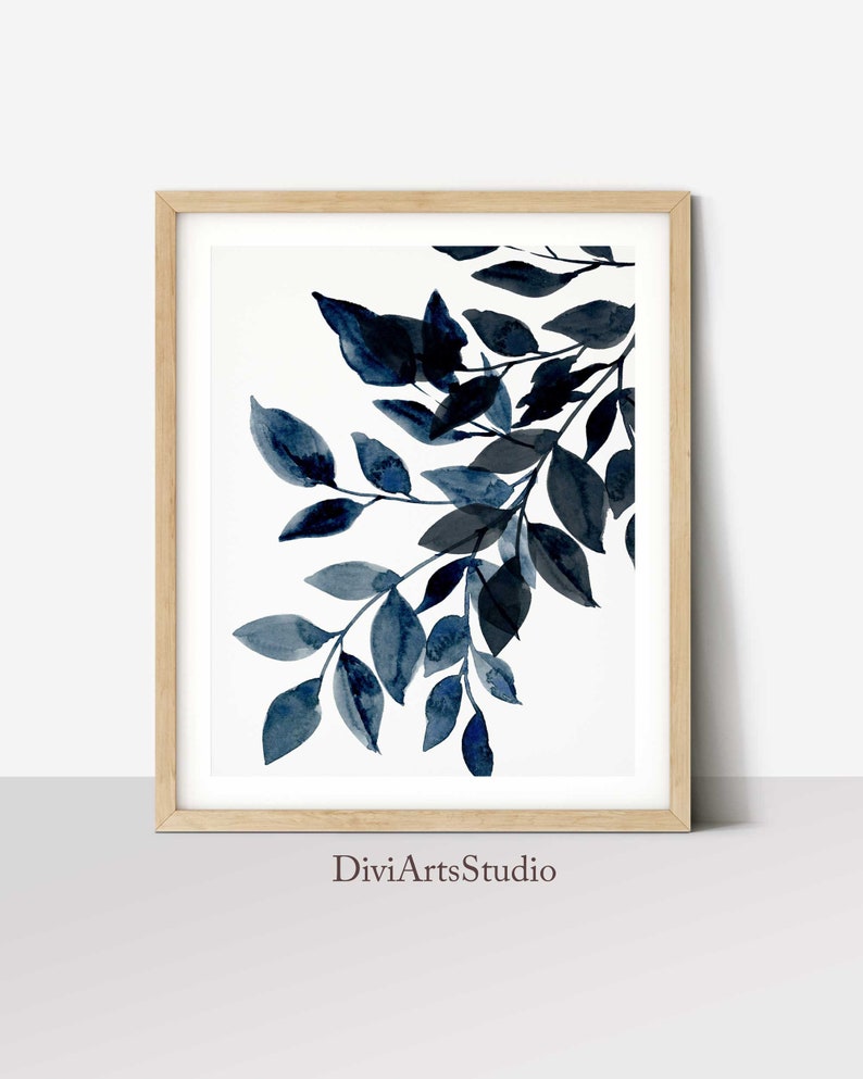 May include: A framed watercolor painting of a branch with blue leaves on a white background. The painting is signed "DiviArtsStudio" in the bottom center.