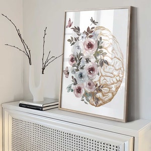 K&ouml;nnte beinhalten: Ein gerahmter Druck eines goldenen anatomischen Gehirns mit Aquarellblumen in Rosa-, Blau- und Gr&uuml;nt&ouml;nen. Die Blumen sind um das Gehirn herum angeordnet und bilden ein wundersch&ouml;nes und einzigartiges Design.