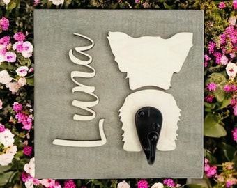 May include: A gray wooden sign with a white silhouette of a dog's rear end and a black hook. The name "Luna" is written in white cursive on the sign.