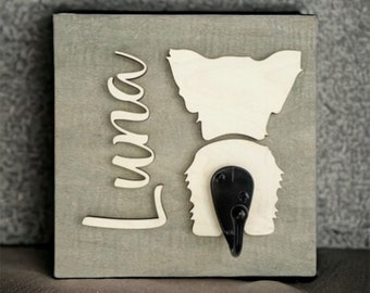 May include: A wooden sign with a white silhouette of a dog's rear end and a black hook. The name "Luna" is written in cursive on the sign.