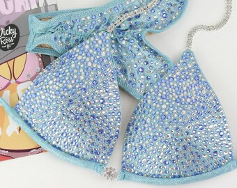 May include: A light blue bikini top and bottom with crystal embellishments. The bikini top has a triangle shape and the bottom has a high-cut style.