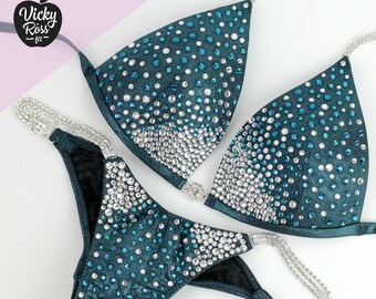May include: Teal and silver sequined bikini competition suit with a gradient design. The suit has a halter top and a high-cut bottom.