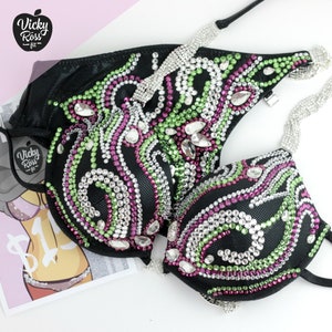 May include: Black bikini top with intricate rhinestone detailing in green, pink, and clear. The design features a swirling pattern of rhinestones. The straps are adorned with silver rhinestones. The brand logo "Vicky Ross fit" is visible.