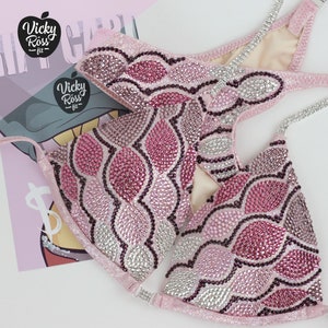 May include: A pink and silver sequined bikini top with a wavy pattern. The top is decorated with rhinestones and has a halter style strap.