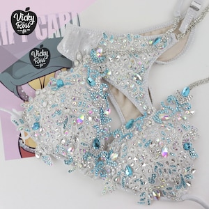 May include: A white and blue embellished dance costume with a floral design. The costume is covered in rhinestones and crystals.