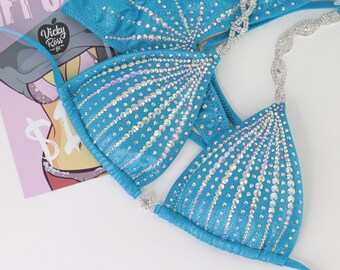 May include: A turquoise bikini with crystal embellishments. The bikini top has a halter style and the bottom is a cheeky cut.