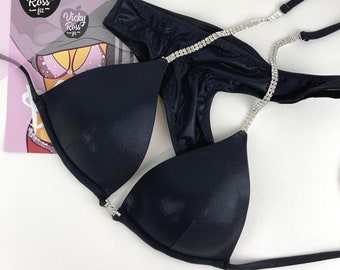 May include: Black bikini set with rhinestone accents. The top features triangle cups and adjustable straps. The bottom is a classic cut. A gift card with the text "Vicky Ross fit" is in the background.