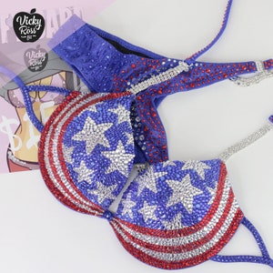 May include: A blue and red bikini with a star-spangled design. The bikini top features a red, white, and blue striped pattern with white stars. The bikini bottom is a solid blue color with a red trim.