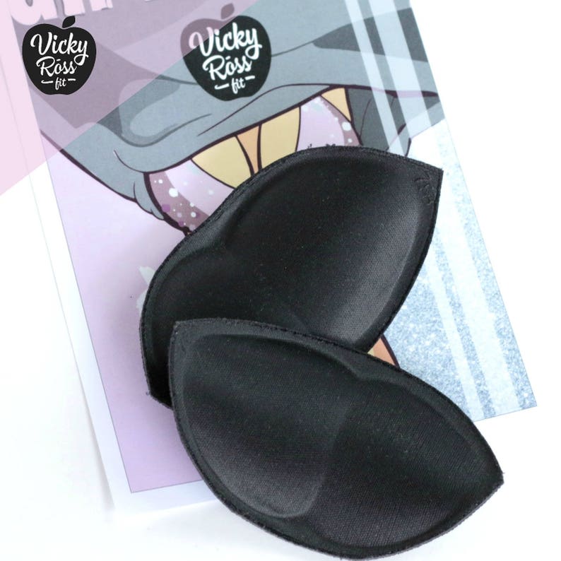 Puede incluir: Dos rellenos de sujetador negros, tambi&eacute;n conocidos como almohadillas push-up, se muestran sobre una superficie blanca. Los rellenos est&aacute;n hechos de un material suave y flexible y tienen una forma redondeada.