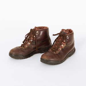 May include: A pair of worn, brown leather hiking boots with dark brown laces and metal eyelets. The boots have a high-top design and a dark sole. The boots are likely vintage and show signs of wear.