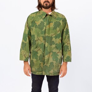 May include: Green camouflage jacket with a leaf pattern. The jacket has a collared neckline, long sleeves, and two front pockets. The jacket is made of a durable fabric and is suitable for outdoor wear. The jacket is a vintage style.